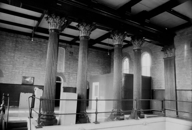 Svartvit bild av ett rum med fyra stora pelare i klassisk stil, med ett högt tak och fönster i bakgrunden.